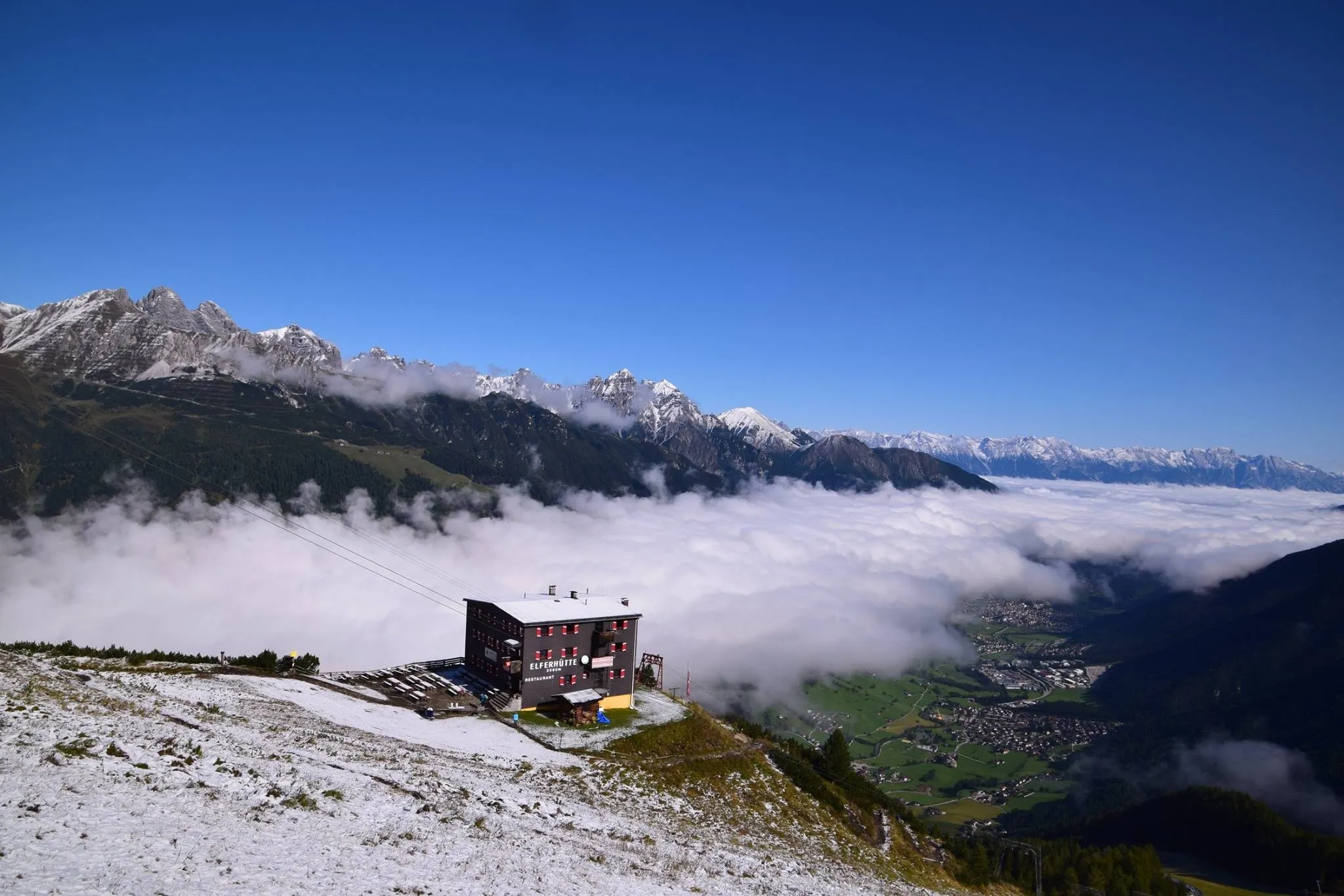 Elferhütte nach dem ersten Schnee über einem Wolkenmeer